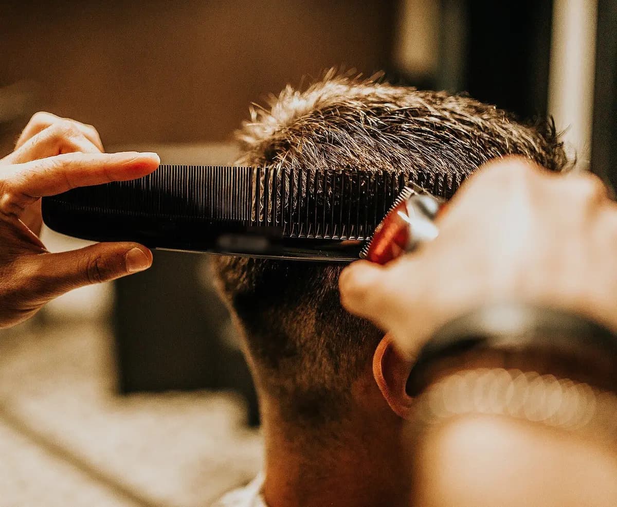 A barber combs and trims a client’s hair, seen from behind